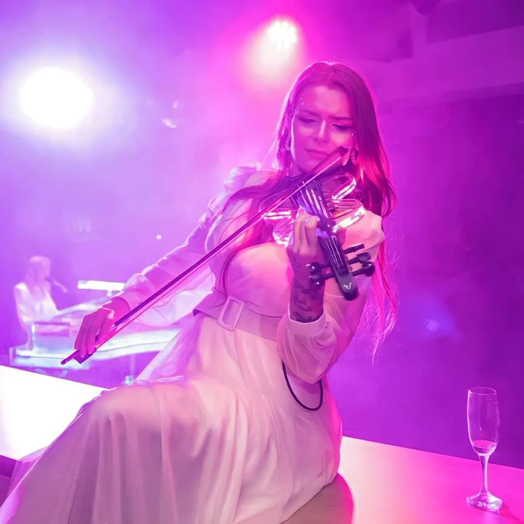 A woman in a dress plays the violin on a grand stage