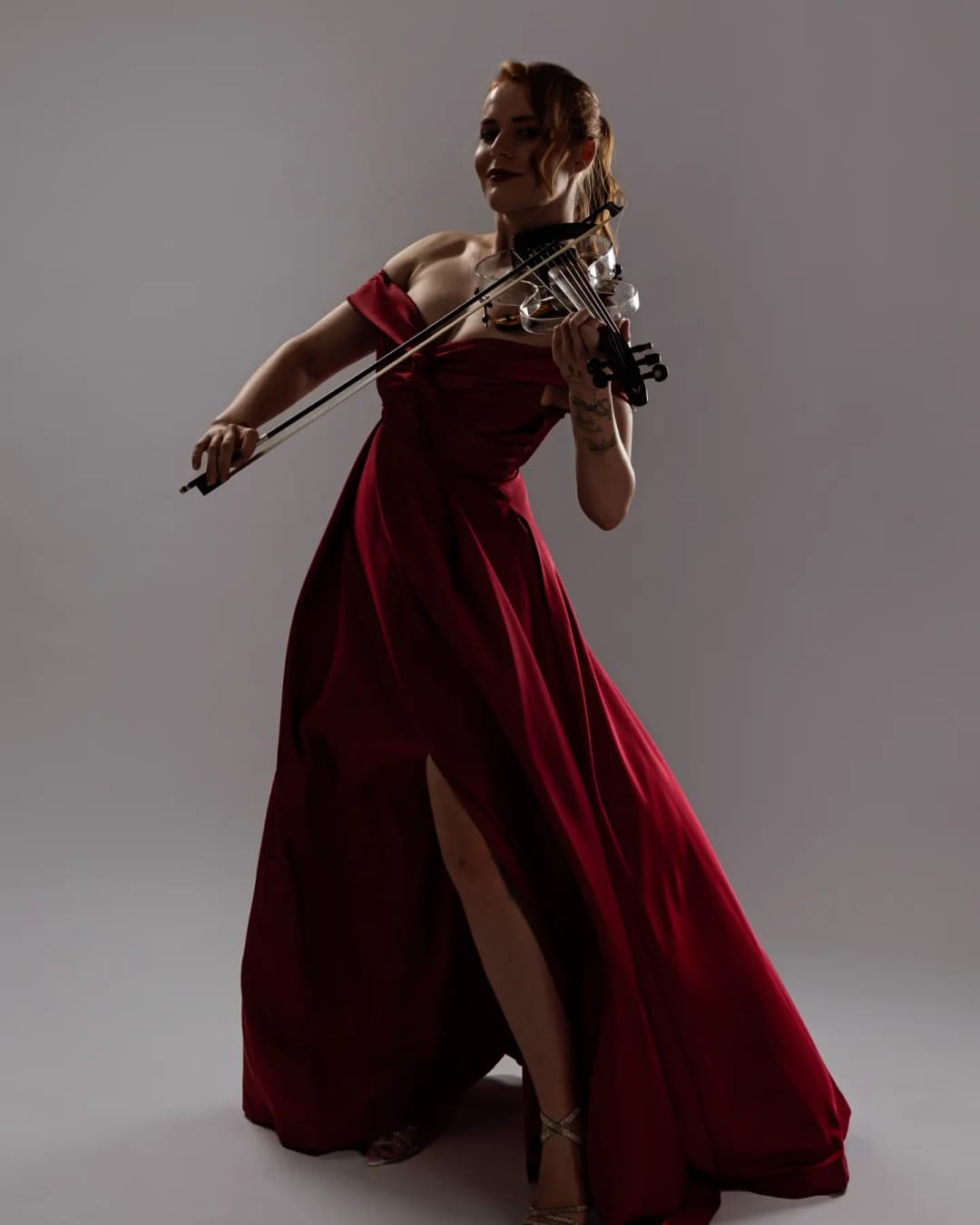 A woman in a beautiful red dress pretends to plays violin