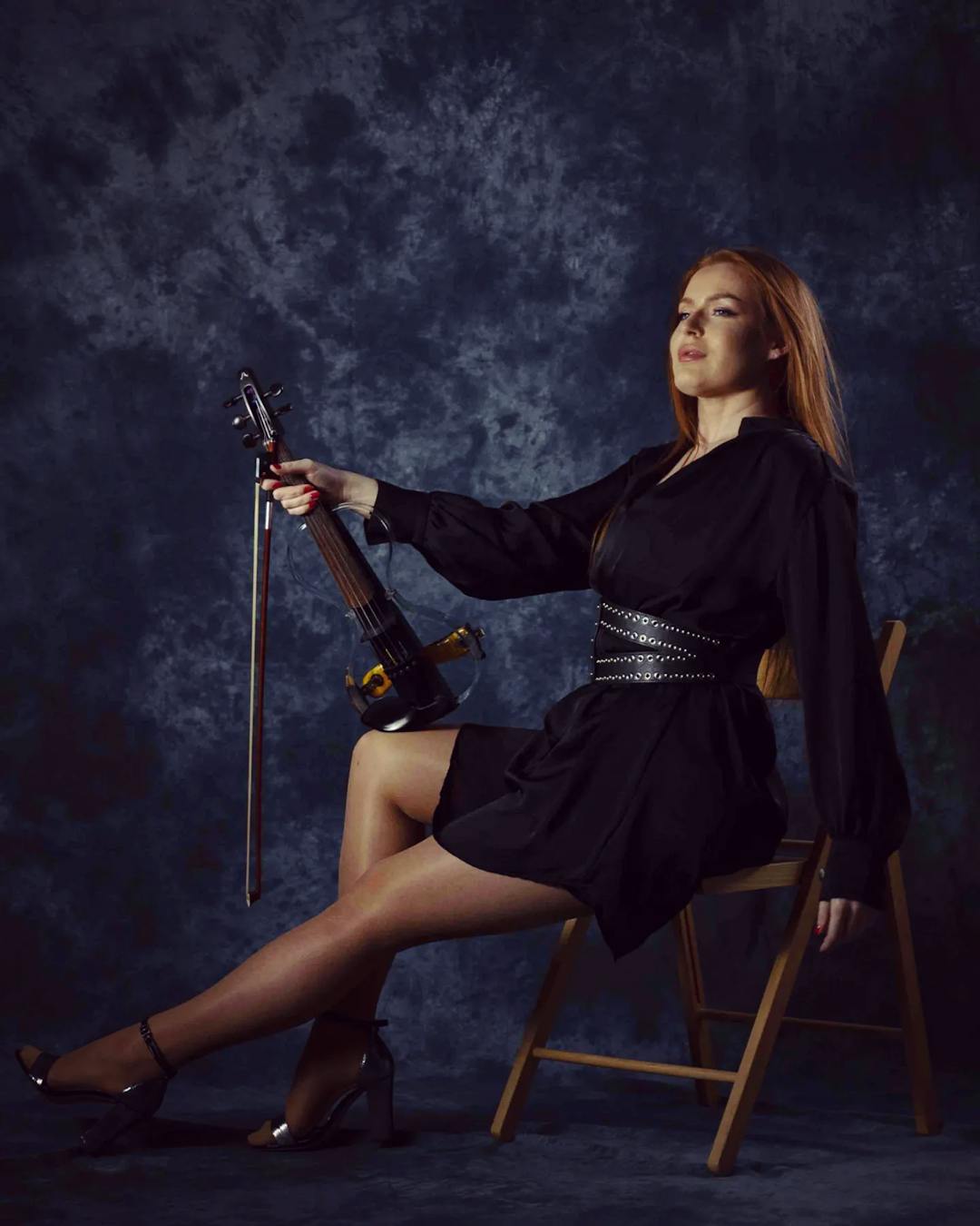 A woman poses with a violin in her hand sitting on a chair