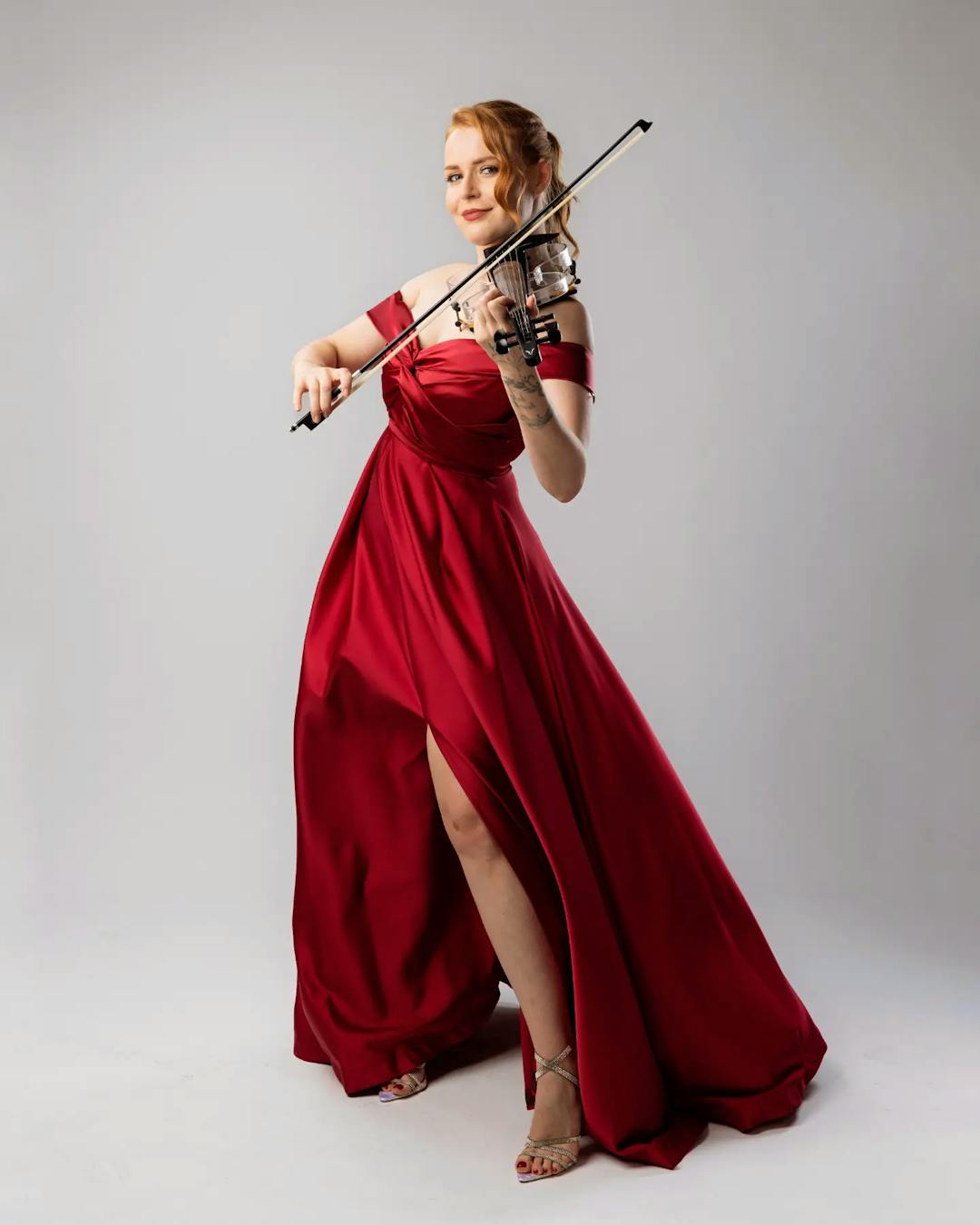 A woman in a beautiful red dress looks at the camera and pretends to plays violin