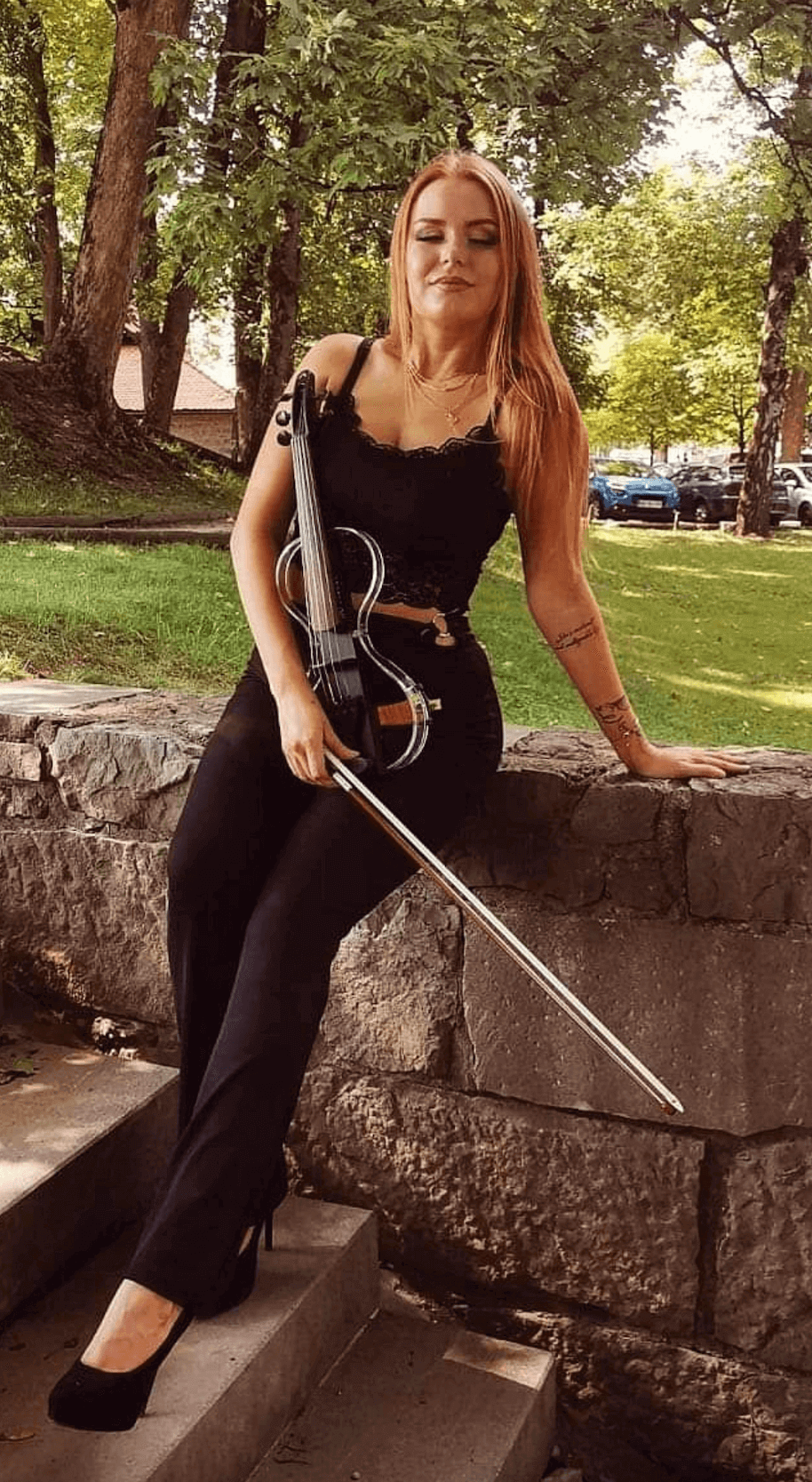 Ekaterina holding violin and sitting on a stone wall